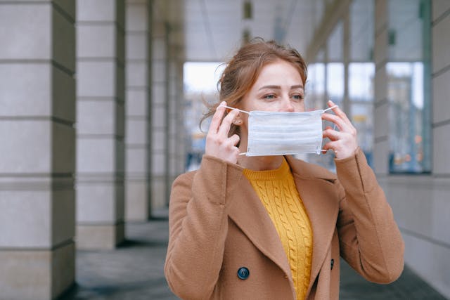 redheaded woman in a yellow sweater putting on a mask